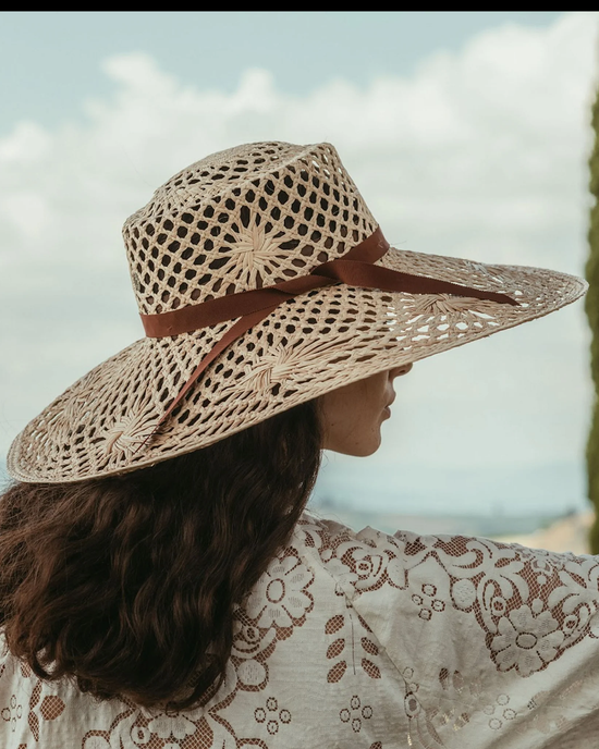 Woman wearing a hand-woven Freya Panama hat in Meringue in Natural/Brown looking out over a landscape.