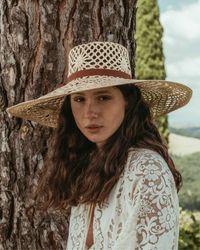 Woman wearing a hand-woven Freya Panama Hat in Natural/Brown standing in front of a tree.