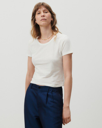 Woman in an American Vintage Gamipy Crop Tee in Blanc and high-waisted denim, pinstriped pants posing for the camera.