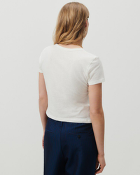 A person viewed from behind, wearing a Gamipy Crop Tee in Blanc made of organic cotton by American Vintage and blue high waisted denim trousers with a pinstripe pattern.