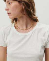 Woman in an American Vintage Gamipy Crop Tee in Blanc looking to the side with a subtle expression, wearing a delicate chain necklace.