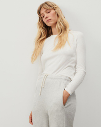 Woman in an American Vintage Gamipy L/S Top in Blanc made of organic cotton and gray sweatpants standing with hand in pocket.
