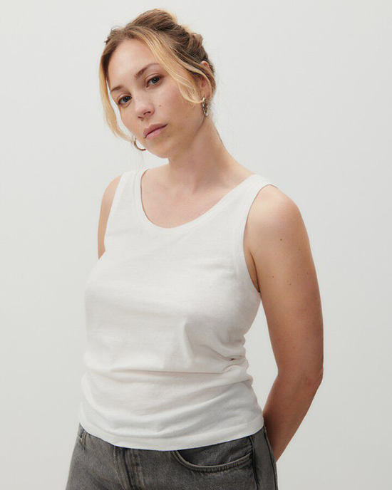 A woman in an American Vintage Gamipy Scoop Tank in Blanc and grey pants, standing with one hand on her hip.