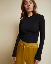 Woman in a Nation LTD Gina Slim Mock Neck in Jet Black and yellow trousers posing against a neutral background.