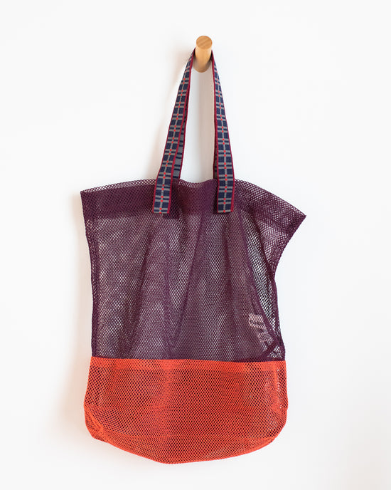 A burgundy and red Large Mesh Bag by Épice hanging on a wooden peg against a white background.