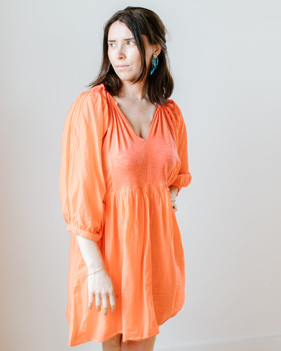 A woman in an orange Erin Shirred Waist L/S Dress in Dolly by Velvet by Graham & Spencer, with silk sleeves and skirt, looks to her right with a neutral expression.