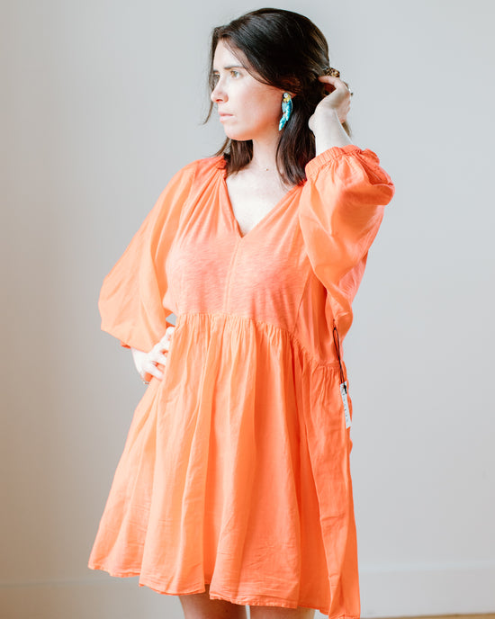 A woman in an orange Velvet by Graham & Spencer Erin Shirred Waist L/S Dress in Dolly standing with her hand in her hair.