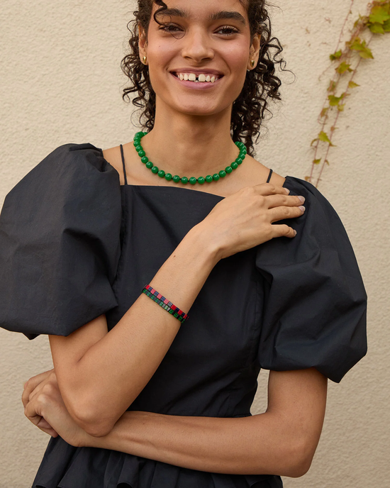 A woman smiling in a black puff-sleeve dress accessorized with a Clare V. Beaded Glass Strand in Emerald and a colorful bracelet.