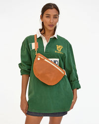 Woman in a green polo dress with a Clare V. Grande Fanny in Cuoio Perf shoulder bag, standing against a white background.