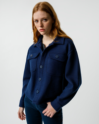 Woman wearing a menswear-inspired blue AMO Halle Shirt Jacket in Neptune against a plain background.