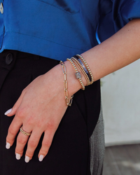 A person wearing Karen Lazar Design's 2MM Sig Bracelet with Blue Sapphire Ombre & Yellow Gold on their wrist and fingers, adorned with 14k Yellow Gold filled beads.