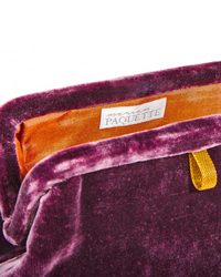 Close-up of a Liette Solid Velvet Clutch in Purple with a "Marian Paquette" brand label.