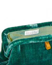 Close-up of a Liette Solid Velvet Clutch in Forest Green evening bag with a brand label "Marian Paquette" inside.