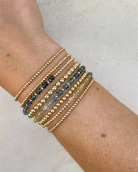 A wrist adorned with multiple bracelets, including the 2MM Sig Bracelet with Laguna Ombre & Yellow Gold beads and a Sapphire gemstone pattern by Karen Lazar Design.