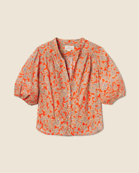 The Loren Blouse in Vermillion Vine by Trovata Birds of Paradis features short puff sleeves, a vibrant orange and beige floral print, v-neckline, gathered shoulders, and a relaxed 100% cotton fit. Shown flat on a light neutral background.