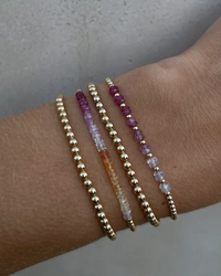 A person's wrist adorned with four Karen Lazar Design 2MM Sig Bracelets with Passion Ombre & Yellow Gold, two featuring 14k Yellow Gold filled beads and the other two with a gradient of purple to clear crystals.