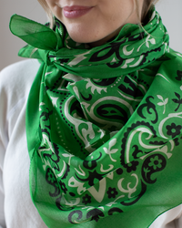 A person elegantly drapes a Maison Lecomte Flament Classic Cotton Bandana in Vert, showcasing its soft cotton voile and distinctive green pattern around their neck and shoulders.