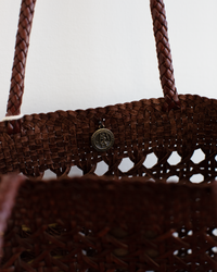 Close-up of the Eclipse Bag in Bruciato by Dragon Diffusion, a brown woven buffalo leather bag with braided handles and a round metallic emblem on the front.