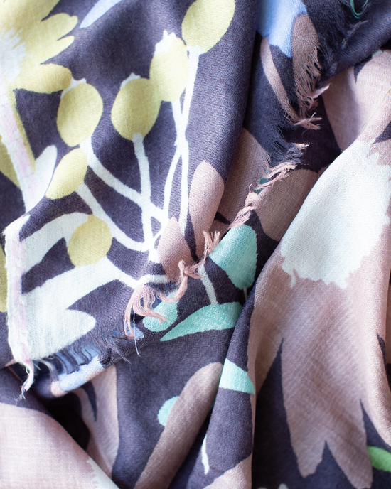 A close-up of the Épice Bold Daisy Wool Silk & Cashmere Scarf in Plum, showcasing its hand-printed floral design with frayed edges and visible threads.