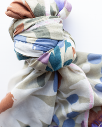 A close-up of the Épice Bold Daisy Wool Silk & Cashmere Scarf in Taupe, featuring a colorful abstract pattern, shown tied loosely against a white background.