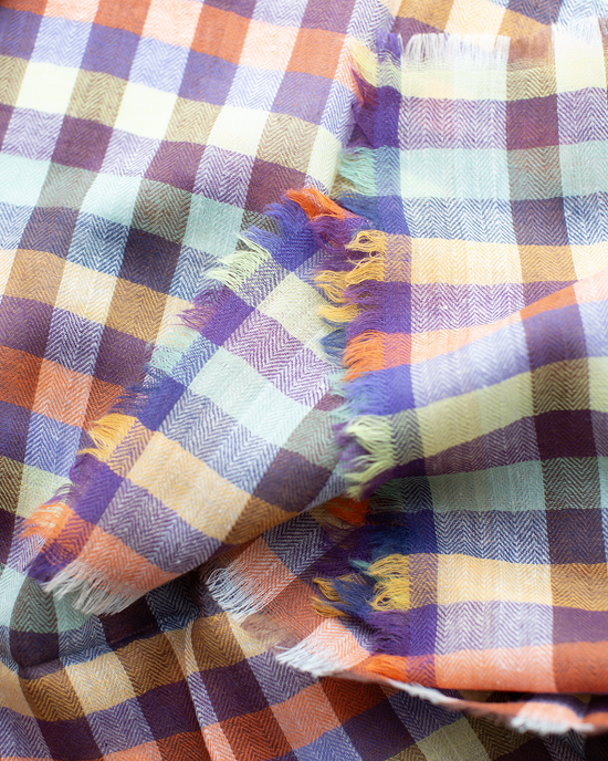 A close-up of the Épice Plaid Wool Bandana in Orange, showcasing its multicolored herringbone plaid pattern and frayed edges.