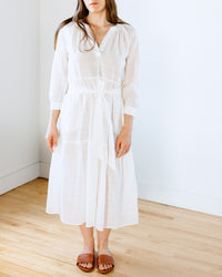 Woman in a Felicite Apparel Puff Sleeve Maxi Dress in White and brown sandals standing against a white wall.