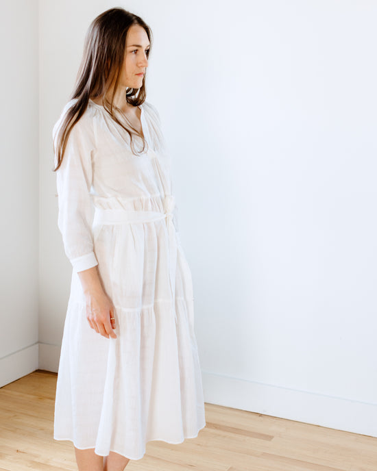 A woman in a Felicite Apparel Puff Sleeve Maxi Dress in White standing against a plain background, looking to the side.