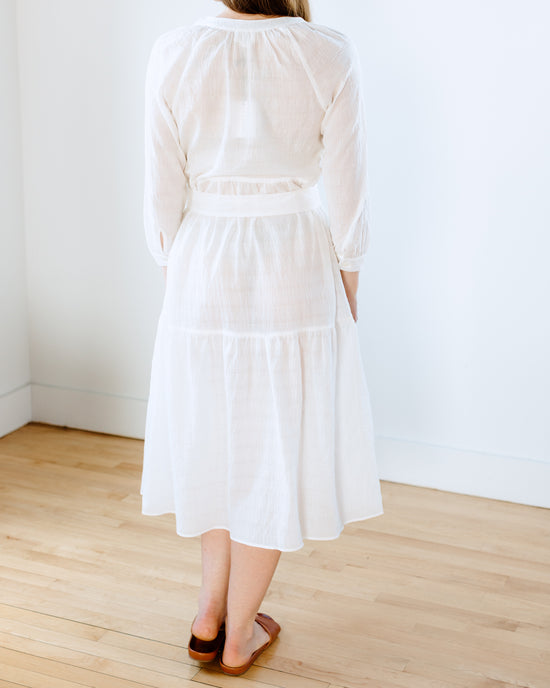 Woman standing in a room wearing a white cotton Felicite Apparel Puff Sleeve Maxi Dress and brown shoes, viewed from behind.