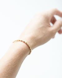 A close-up of a wrist adorned with a delicate enewton Gold Harmony Grateful Pattern 2mm Bead bracelet, featuring 14k gold filled beads against a white background.