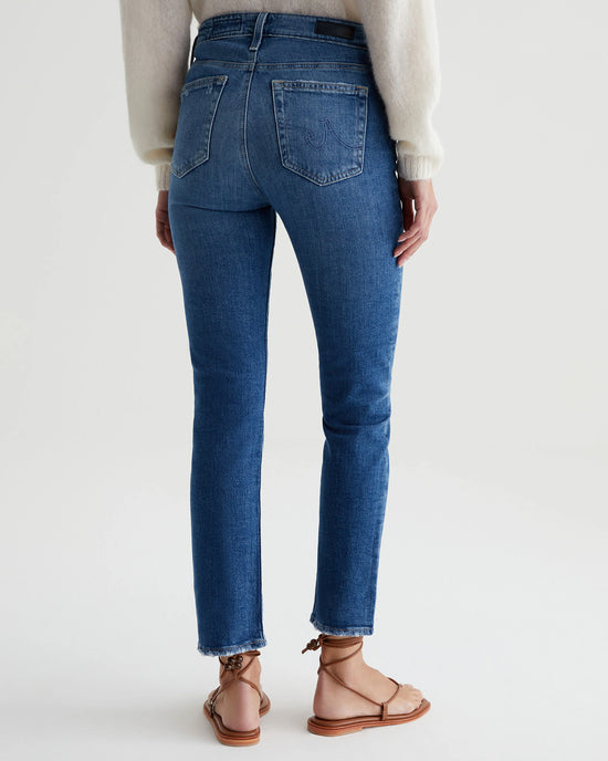 Woman in AG Jeans Mari Crop in Alibi Destructed straight leg jeans and brown sandals viewed from the back, standing against a plain white background.