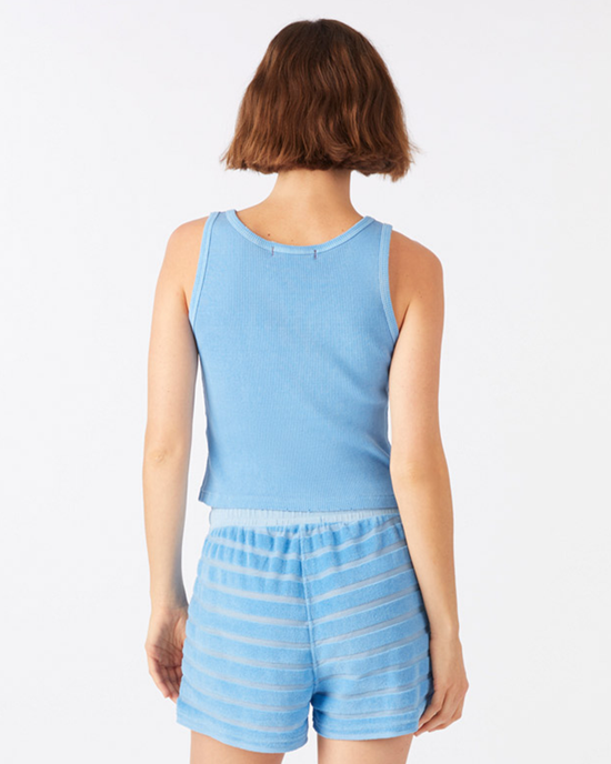 Woman from behind wearing a light blue Crop Rib Tank in Tranquil by AMO and striped blue shorts standing against a plain background.