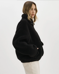 A woman in a black Lamarque Kim Jacket in Black Sherpa looking over her shoulder against a white background.