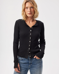 A woman wearing an AMO Lacy Rib Cardigan in Black and blue jeans standing with one hand in her pocket.