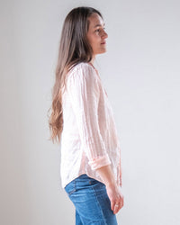 A woman with long brown hair stands in profile against a plain light background, wearing the LLEA BLUE Carrie Fitted Blouse in Bermuda Sand Linen and blue jeans.
