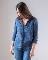 A person with long brown hair models the LLEA BLUE Carrie Fitted Blouse in Moonlit Ocean Linen and blue jeans, standing against a plain light background with arms relaxed at their sides.