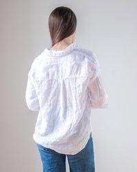 A person with long brown hair wears the LLEA BLUE Alix Top in White Linen and blue jeans, standing with their back to the camera against a plain light background.