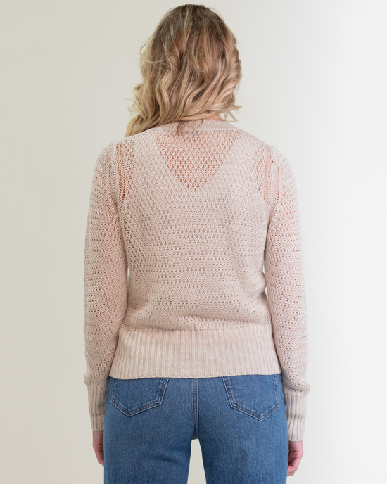 Woman standing with her back to the camera, wearing a pink Margaret O'Leary Elodie Cardigan in Natural and blue jeans.
