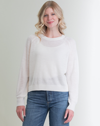 A smiling woman with blonde hair, wearing a Margaret O'Leary Rib Linen PO in White and blue jeans, standing against a plain background.