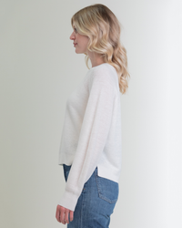 Profile view of a woman with blonde wavy hair wearing a Margaret O'Leary Rib Linen PO in White and blue jeans, standing against a light gray background.