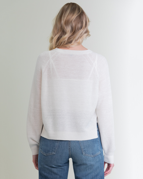 Woman facing away from the camera, wearing a Margaret O'Leary Rib Linen PO in White and blue jeans, standing against a plain background.