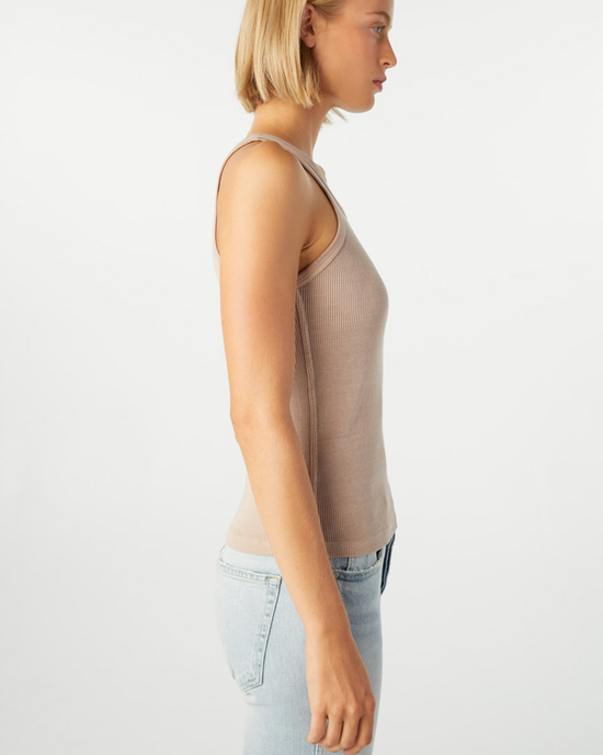 Profile view of a woman wearing an AMO Long Rib Tank in Taupe and light blue jeans against a white background.