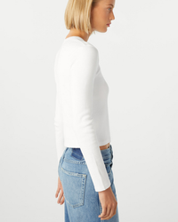 Woman wearing an AMO Slim Rib Tee in White and blue jeans, showing side profile.