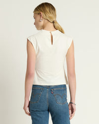 A person with long blonde hair in a low ponytail is standing and facing away, wearing the Nation LTD Lulu Mock Neck Top in Porcelain paired with high-waisted blue jeans.