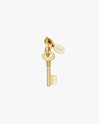 An antique brass key with an attached oval tag inscribed with the word "clarity," featuring vintage gold plating: The Le Cle Charm in Vintage Gold by Clare V.