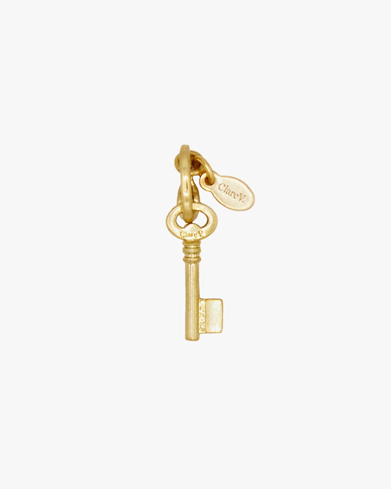 An antique brass key with an attached oval tag inscribed with the word "clarity," featuring vintage gold plating: The Le Cle Charm in Vintage Gold by Clare V.