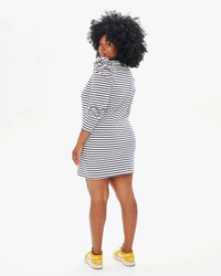 A woman in a Le Puff Dress in Navy & Cream Stripe by Clare V. with puff shoulders and yellow sneakers posing with her back partially turned to the camera.
