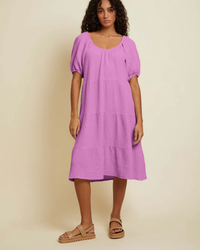 A woman wearing a purple Nation LTD Double Gauze Mindy Peasant Dress in Prom Date and tan sandals.