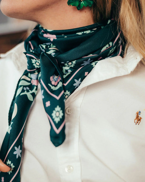 A person wears a white collared shirt, a green flower earring, and the Maison Lecomte Flament Secret Garden 100% Silk in Vert scarf styled as a square bandana around their neck.
