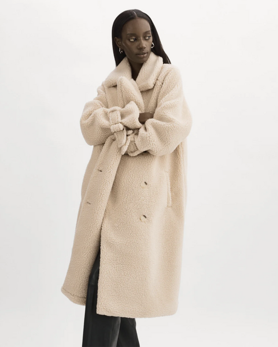 A woman posing in a Lamarque Malani Jacket in Beige, an oversized sherpa coat with double-breasted button closure, against a white backdrop.