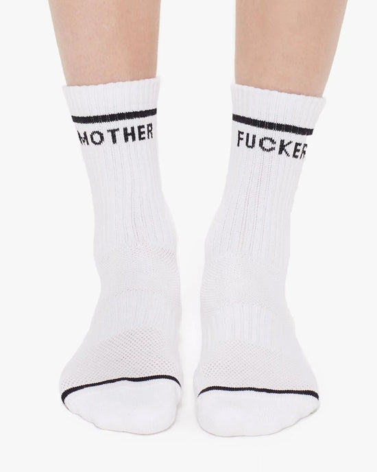 A pair of feet wearing Mother’s MF Baby Steps in White—vintage-inspired tube socks with black stripes and “MOTHER” and “FUCKER” across the top.